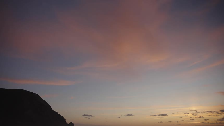 A pastelcolored sky glows at dawn or dusk above a dark mountain silhouette