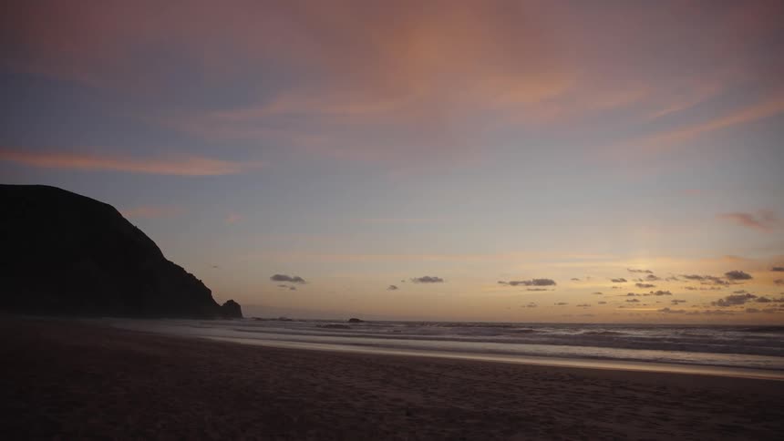 A beach at dawn with a mountainous rock on the side