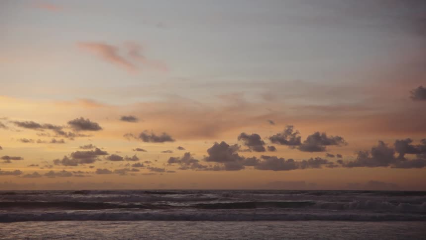 A beach with gentle waves and an orange sky at sunset