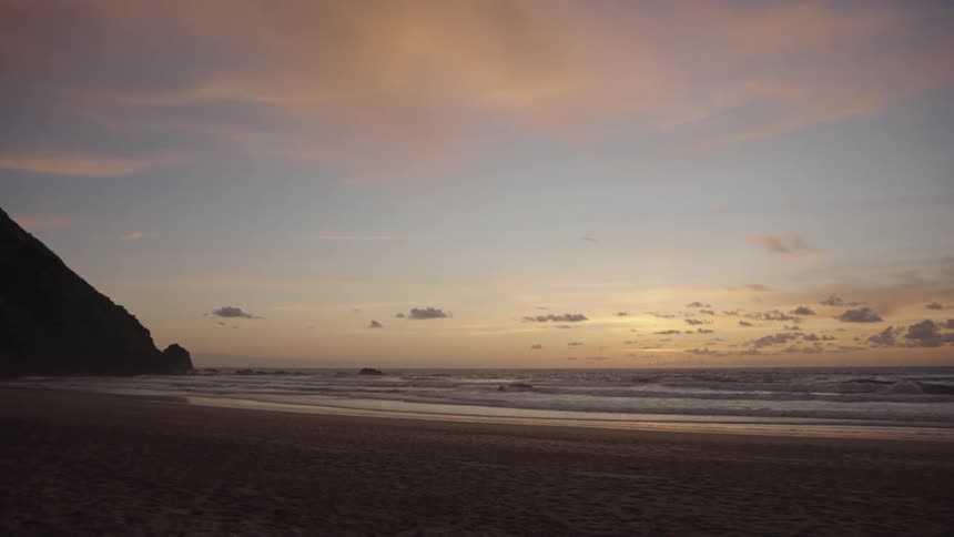 Calm waves flow along a beach under a colorful sunset sky