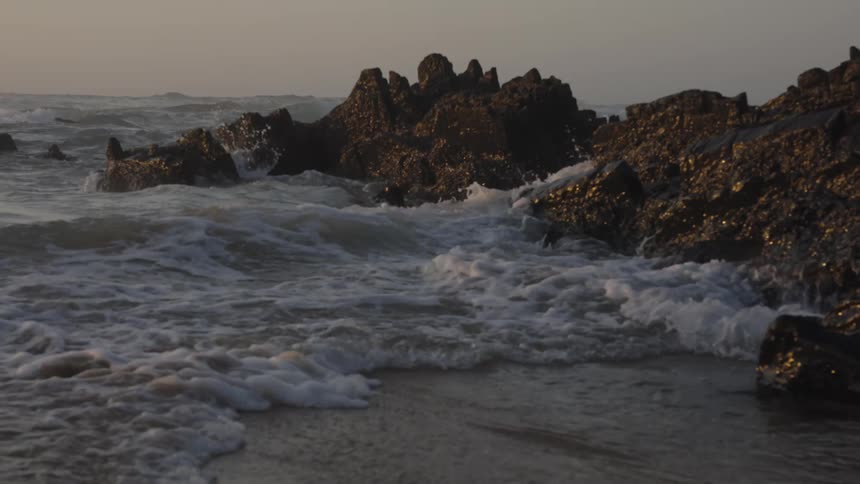 Waves crash against dark rocks at the shoreline