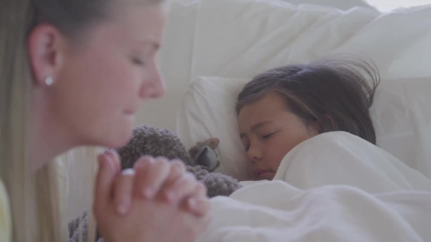 Distressed mother praying for her sick child sleeping on a hospital bed