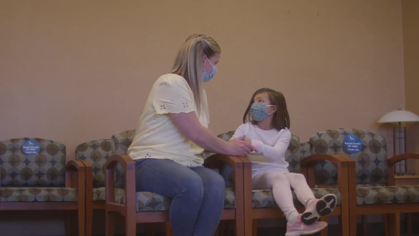 Mother and young daughter anxiously sitting in a doctors waiting room wearing face masks