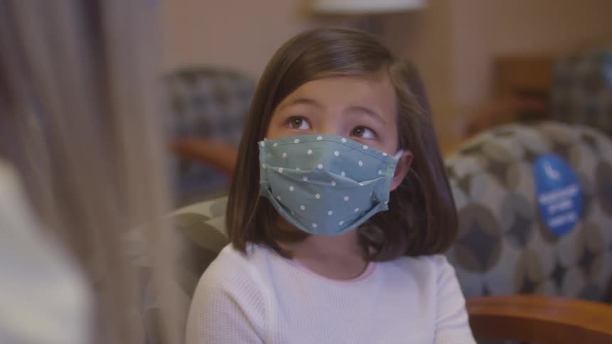Girl wearing a blue polka dot face mask looks upward