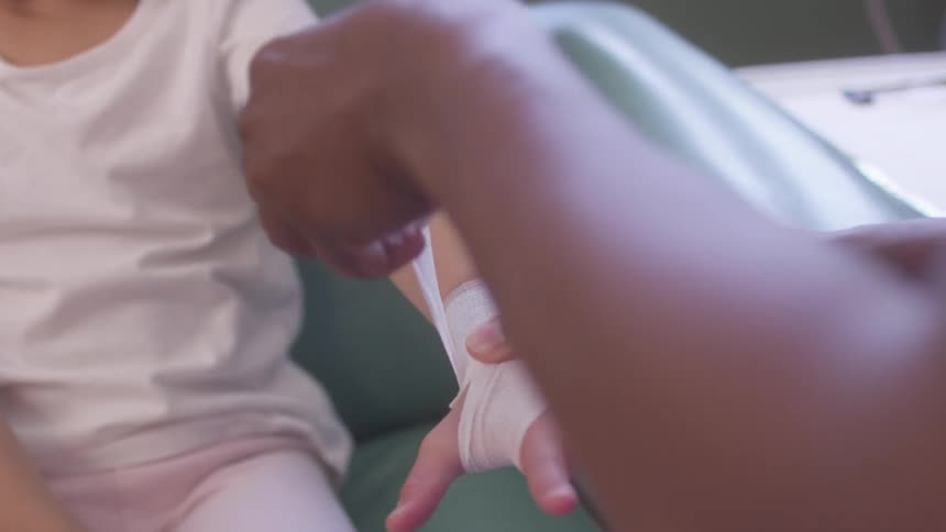 A mans hands gently wrap a bandage around a childs forearm in a medical setting