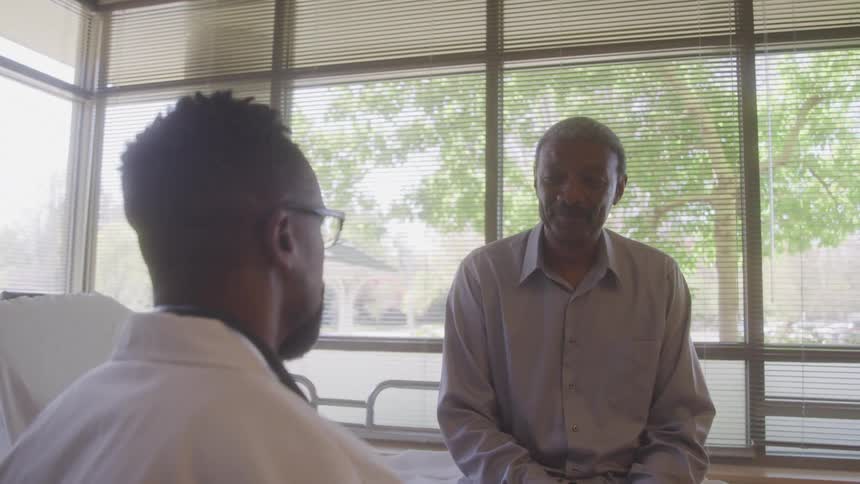 Doctor talks with a patient sitting on the edge of the bed in a bright room
