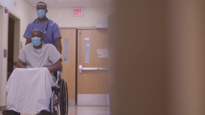Healthcare professional pushing a patient in a wheelchair down a hospital hallway