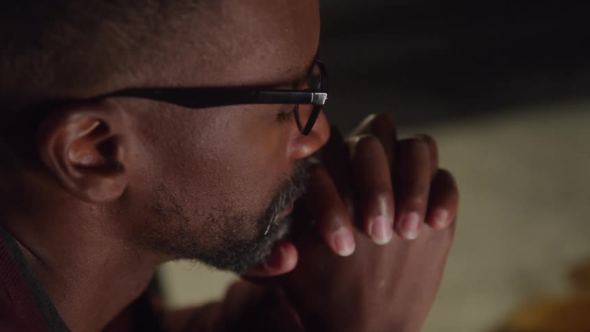 Man wearing glasses with eyes closed and hands clasped in prayer