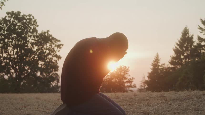 Man kneeling outdoors and placing his hand on his face