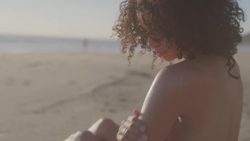 Woman sitting on the beach touching her shoulder