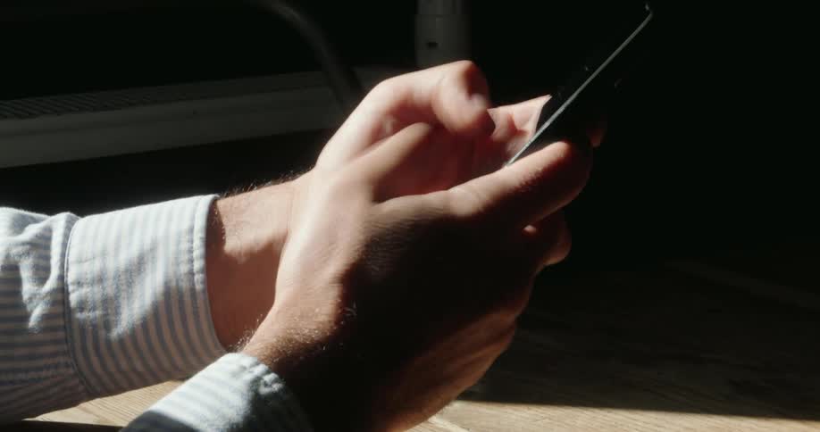 Man texts on a smartphone in an area lit by sunlight