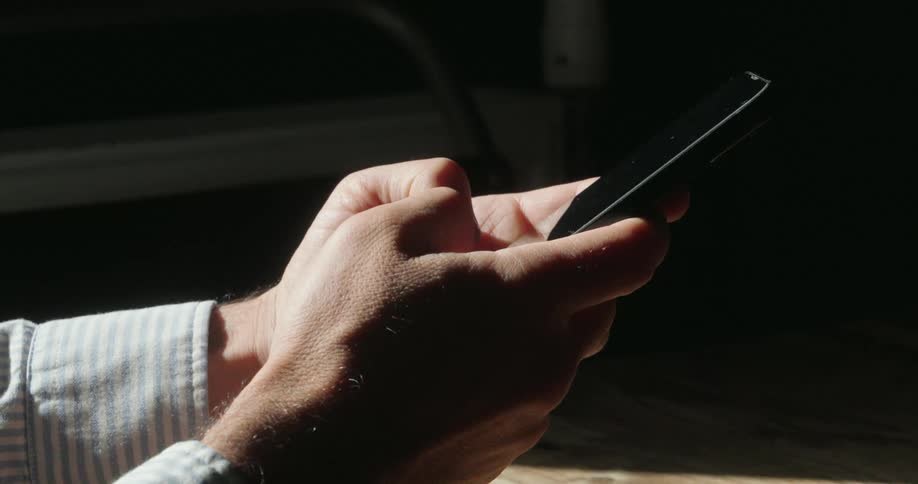 Close up of a young man texting with a mobile phone while seated in a room during daytime