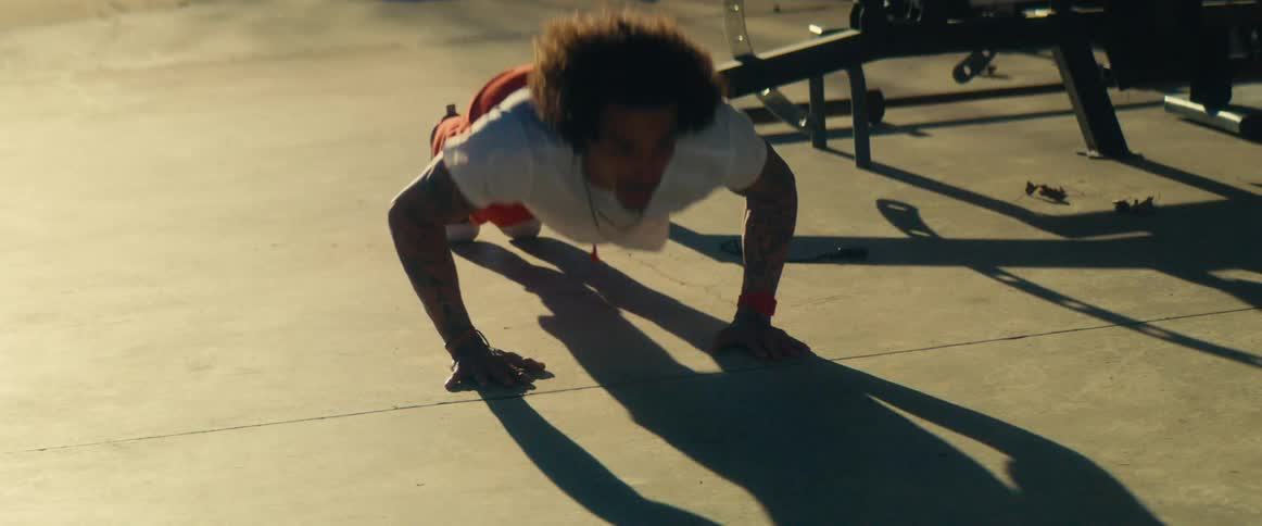 A young black man does push up variations in an outdoor gym area during daytime