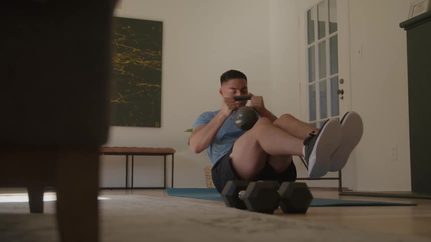 A young man exercises with dumbbells in his living room at midday