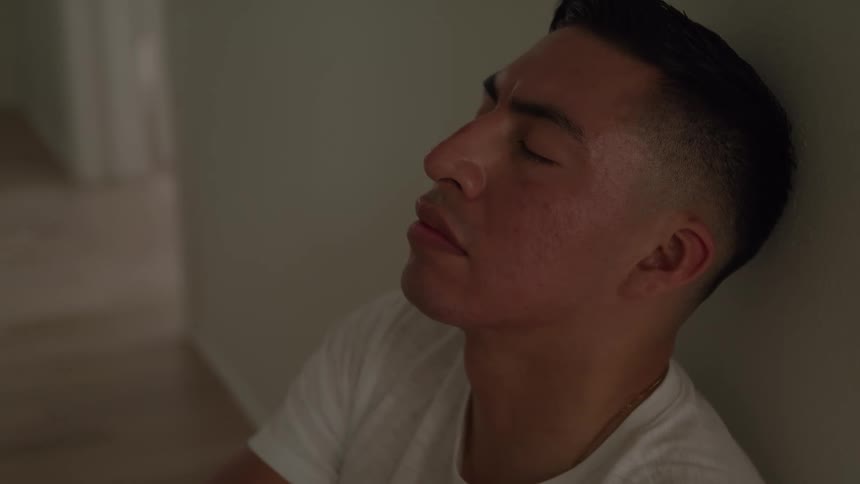 A closeup of a man with his eyes closed leaning against a wall appearing tired or distressed