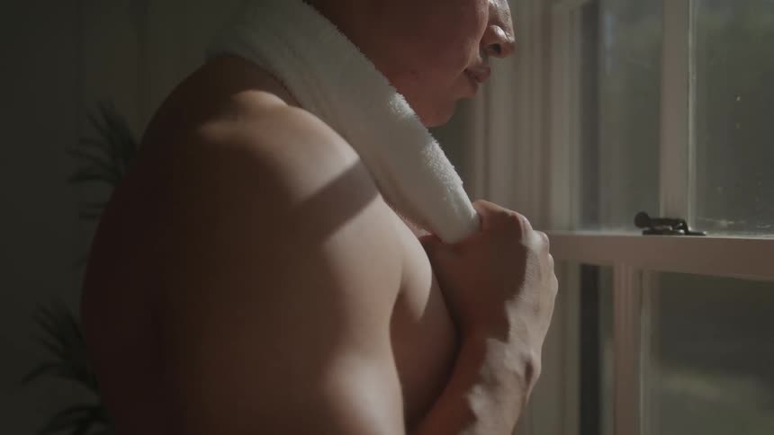 The shirtless man is looking out the window