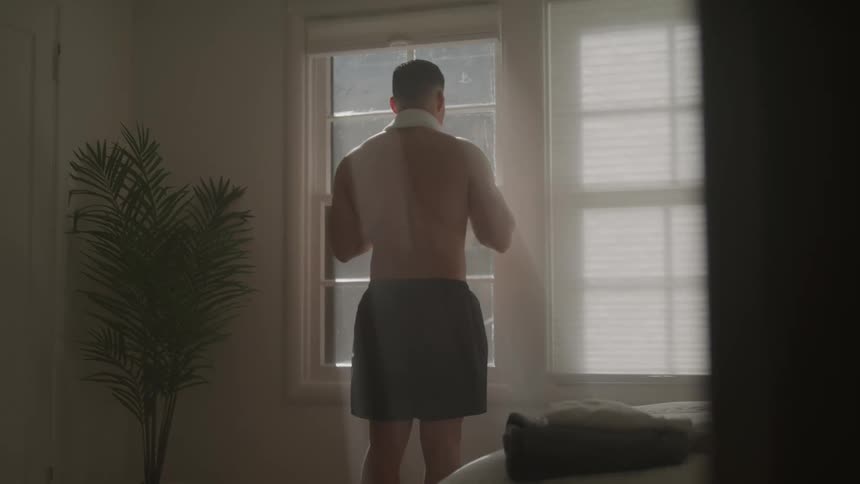 Shirtless man facing a window