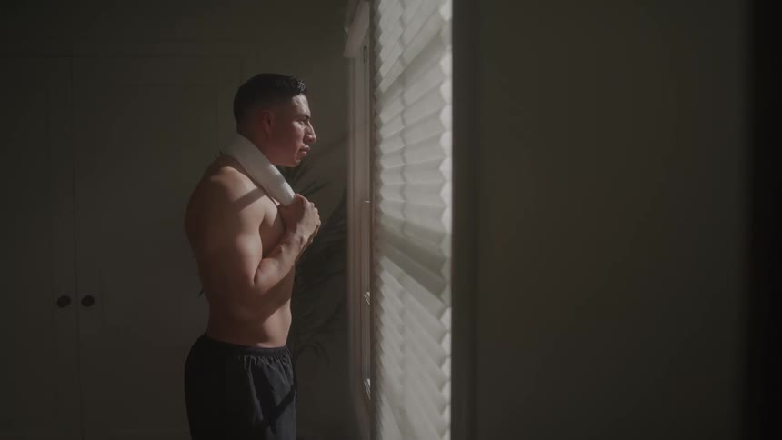 Shirtless man with a towel facing a window