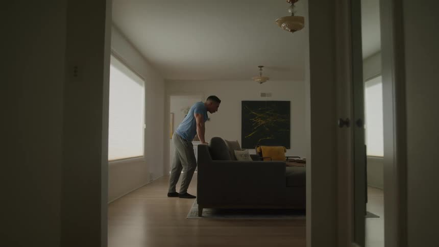 Man leaning over the back of a sofa in a living room lit by natural light