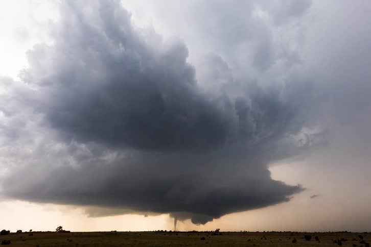 A tornado forms beneath dark storm clouds over open plains