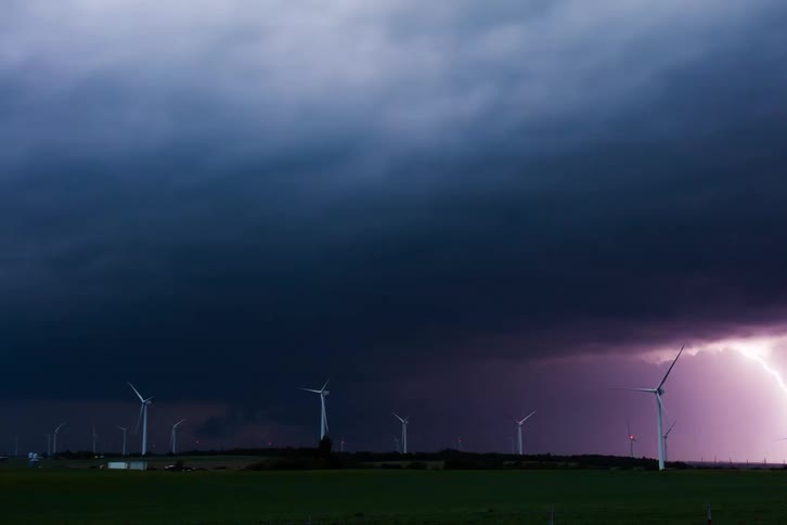 Lightning strikes over wind turbines under dark storm clouds