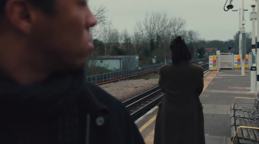 Man with a serious expression looking at a woman with her back turned in an outdoor subway station