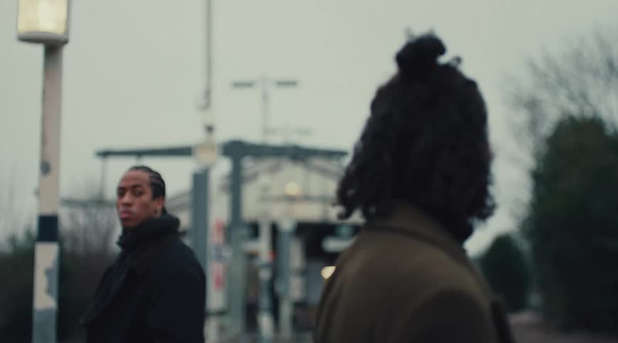 A woman with curly hair looks into the distance then a man turns to look at the woman and finally the woman stares off with a serious expression