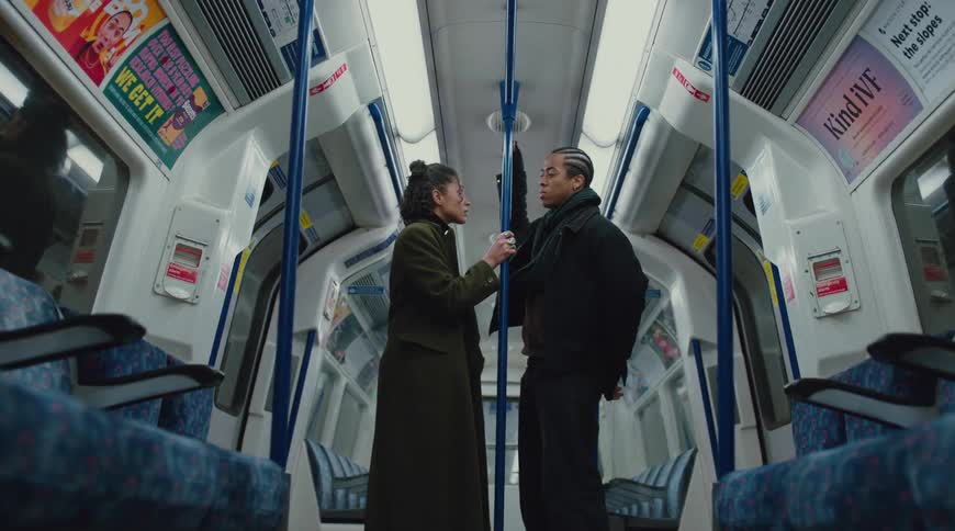 A man and woman stand facing each other inside an empty subway car engaged in conversation