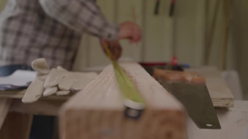 Person marking a wooden plank with a tape measure and pencil