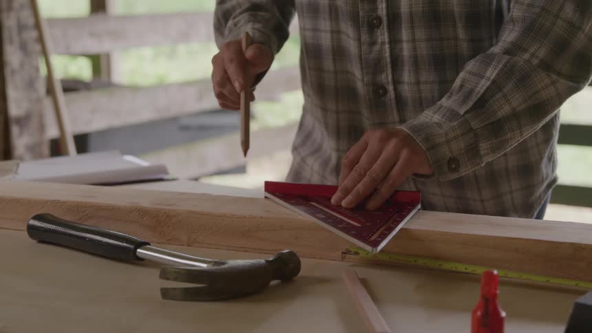 Person marking wood with a square on a carpentry workbench