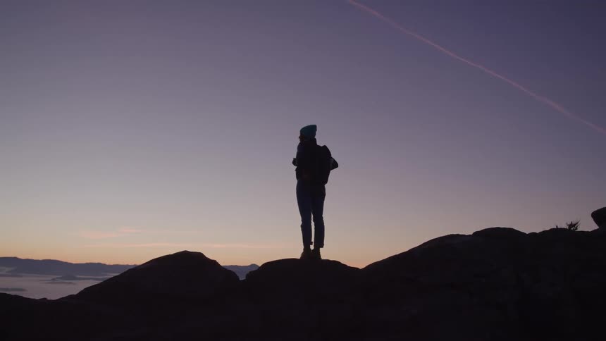 Silhouette of a woman standing on rocks watching the sunrise