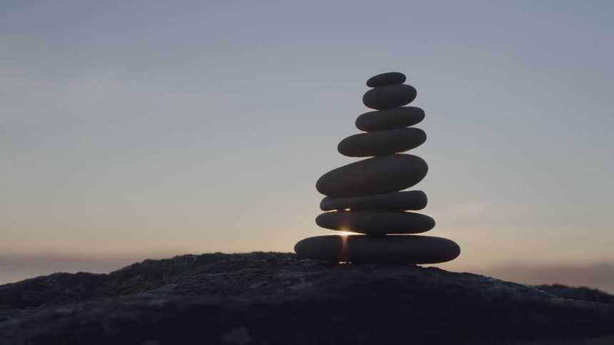Stack of balanced stones on a rocky surface with the sun rising in the background