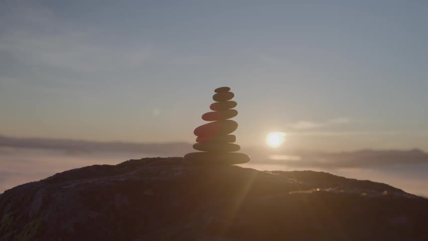 A series of small rocks stacked into a pyramid on a hill blocking the setting sun