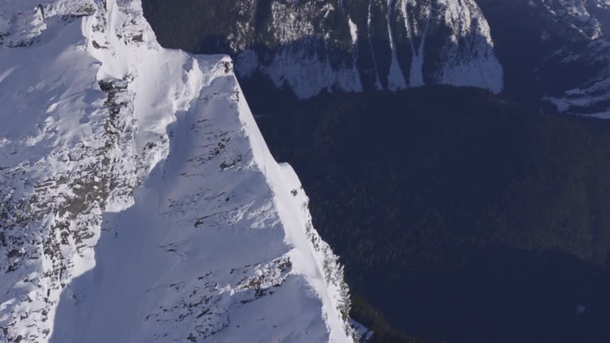 A sharp snowcovered mountain ridge rises dramatically above dark forested valleys