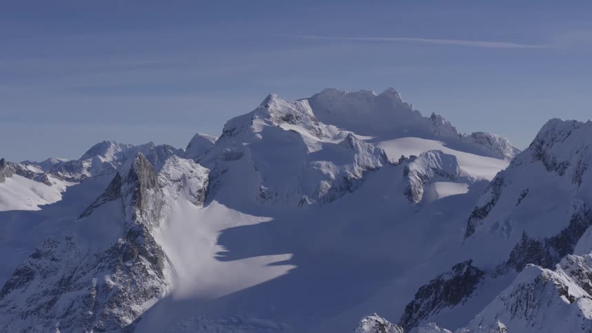 A range of towering snowcovered mountains glistens under a clear blue sky