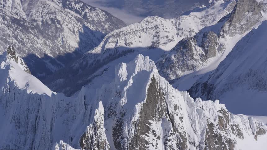 A rugged snowcovered mountain peaks and jagged ridges under a hazy sky