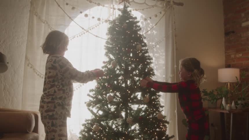 Two children decorating a christmas tree in the living room