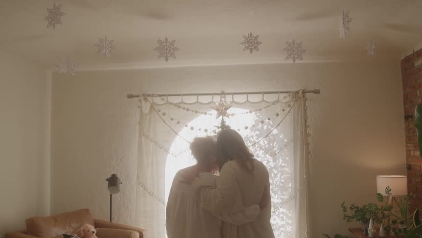Two people embracing in front of a window decorated with snowflakes