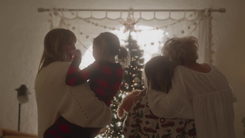 Two women holding children in front of the lit christmas tree