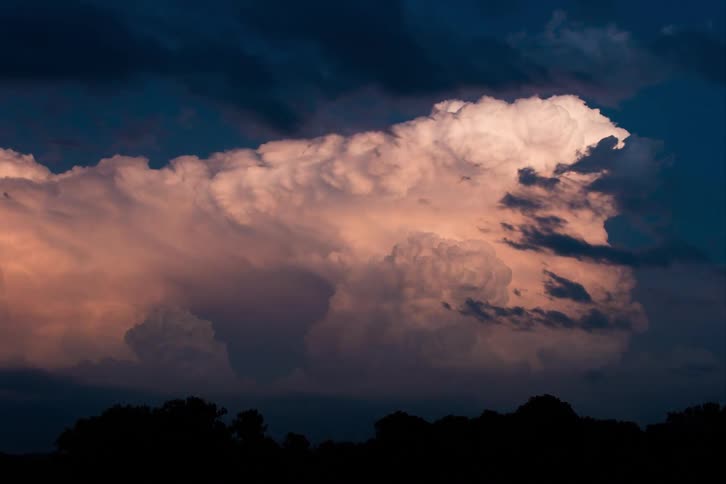 A massive thunderstorm cloud flashes with lightning at dusk