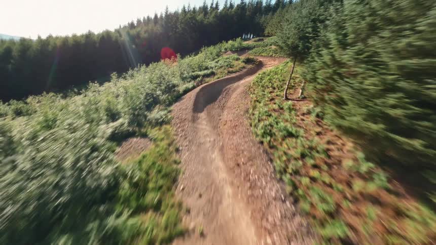 The video shows a winding dirt trail through a forest filmed from an aerial view the camera flies over a trail that passes through both a grassy hilly area and a dense forest