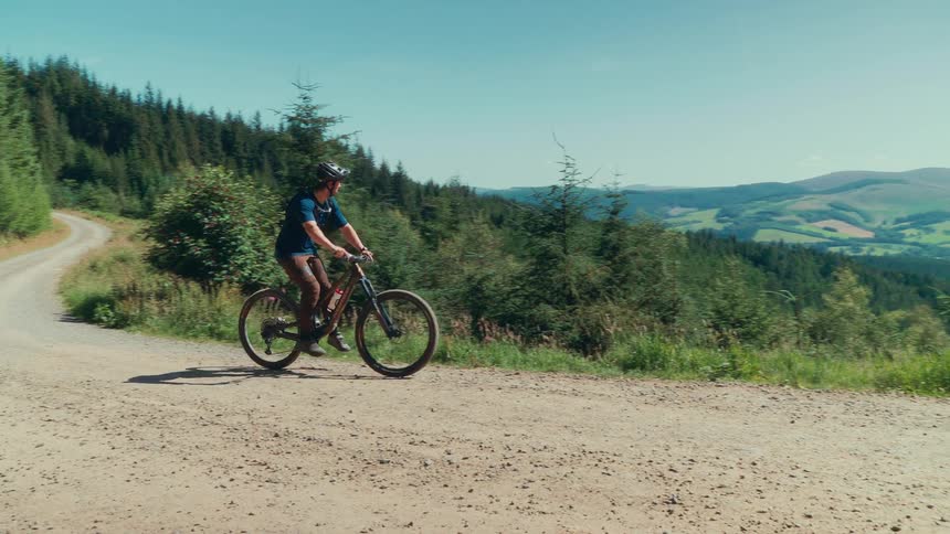 A man bikes on a hillside dirt road enjoying the view