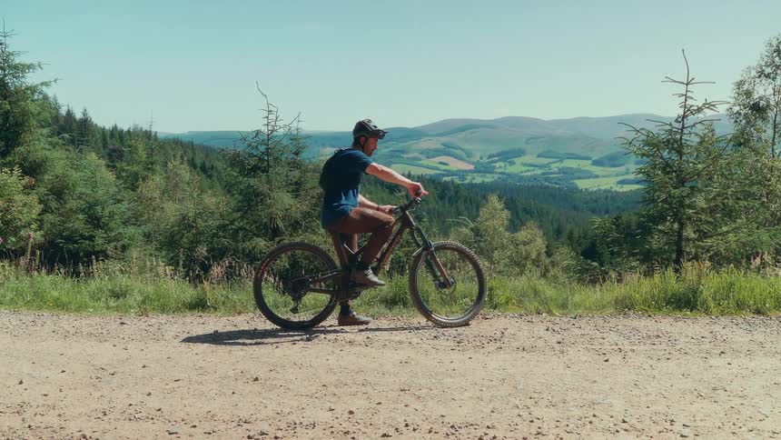 Man putting on helmet and starting to cycle while in mountainous environment