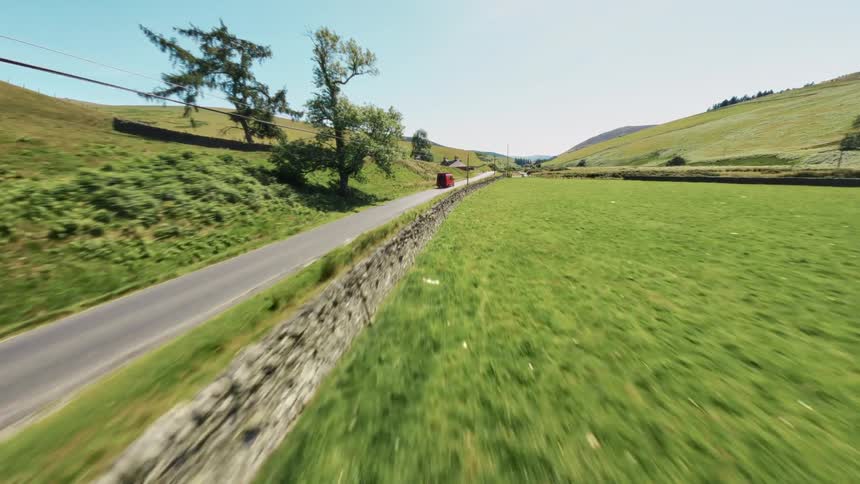 A van drives down a narrow rural road through open countryside