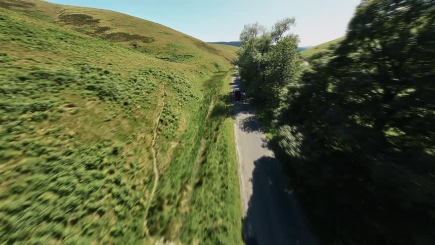 A red delivery van drives on a highway lined with hills and trees at midday