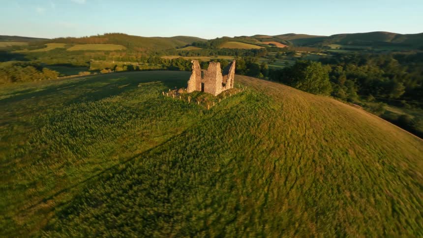 A drone orbits around a grassy hilltop with large stones at sunset