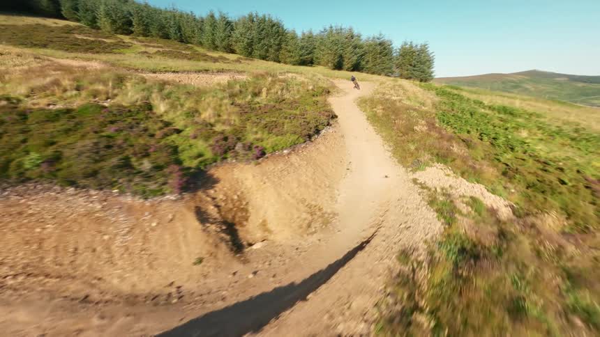 Cyclist rides down a dirt trail through green hills