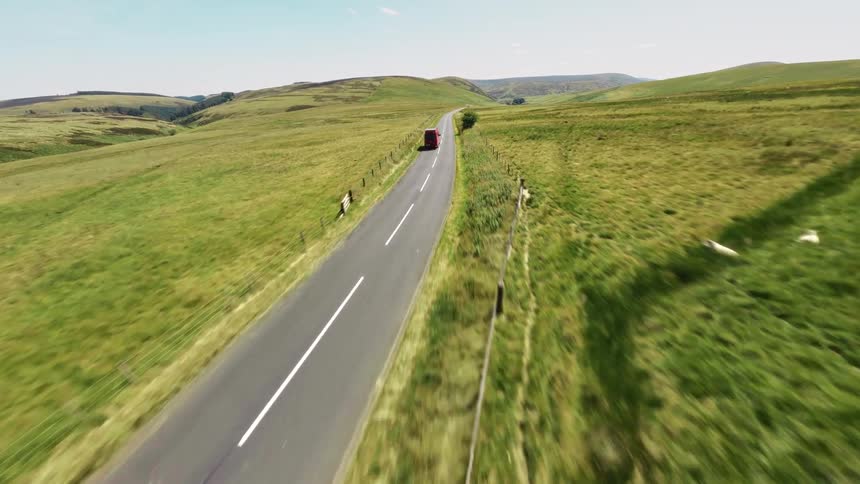 Red van driving along a narrow road between open fields