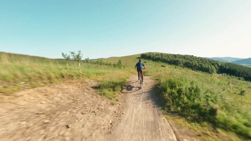 Cyclist rides down a winding trail among green hills