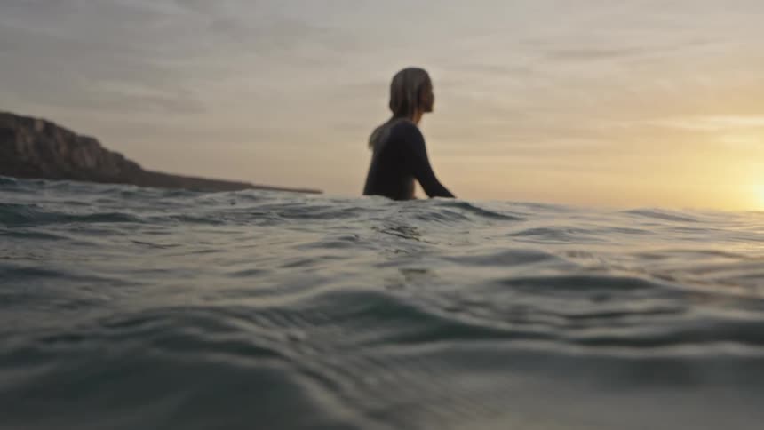 Surfer sitting on the board watching the sunset at sea